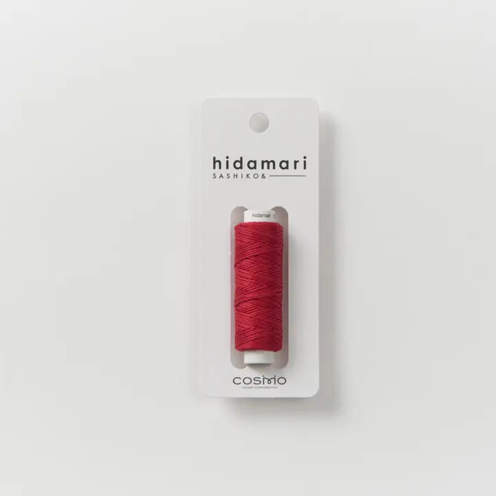 A single spool of red sewing thread mounted on a white card, with the brand name 'hidamari' and 'SASHIKO' printed above and 'cosmio' below, set against a clean white background.