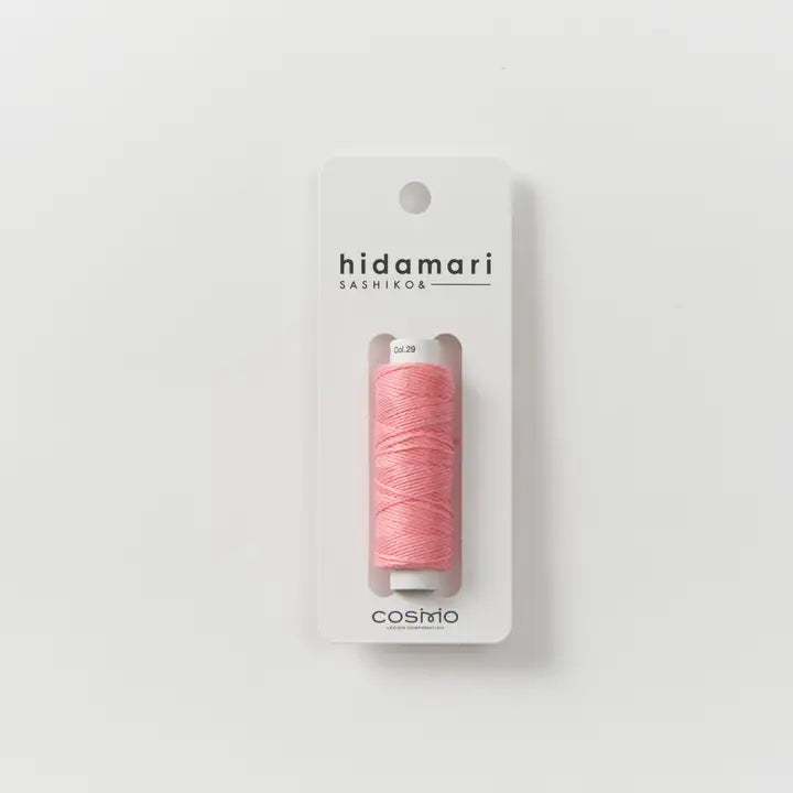 A spool of pink sewing thread in a white plastic casing, mounted on a white cardboard backing card. The backing card features the brand name 'hidamari' and the line 'SASHIKO6', with the size '50.